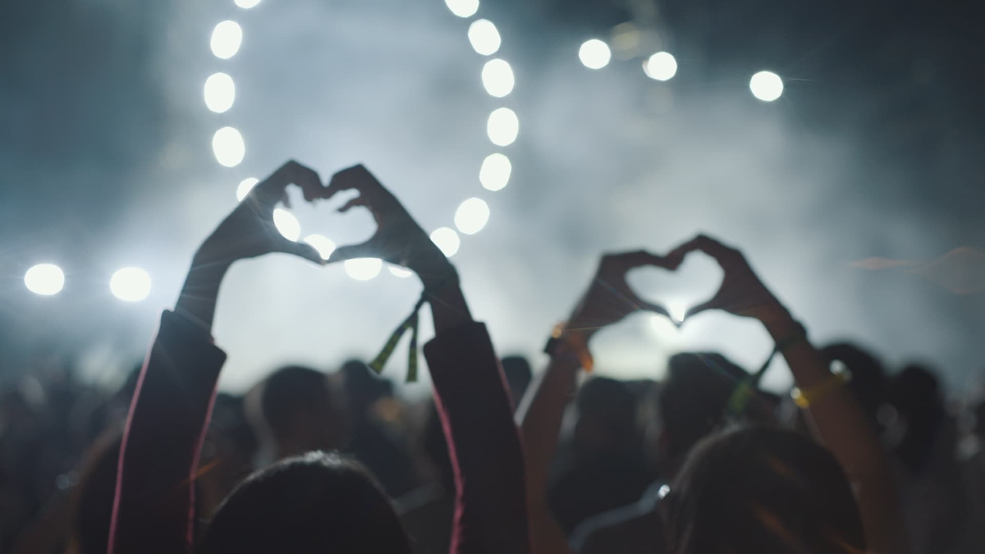 Público de un concierto formando un corazón con las manos