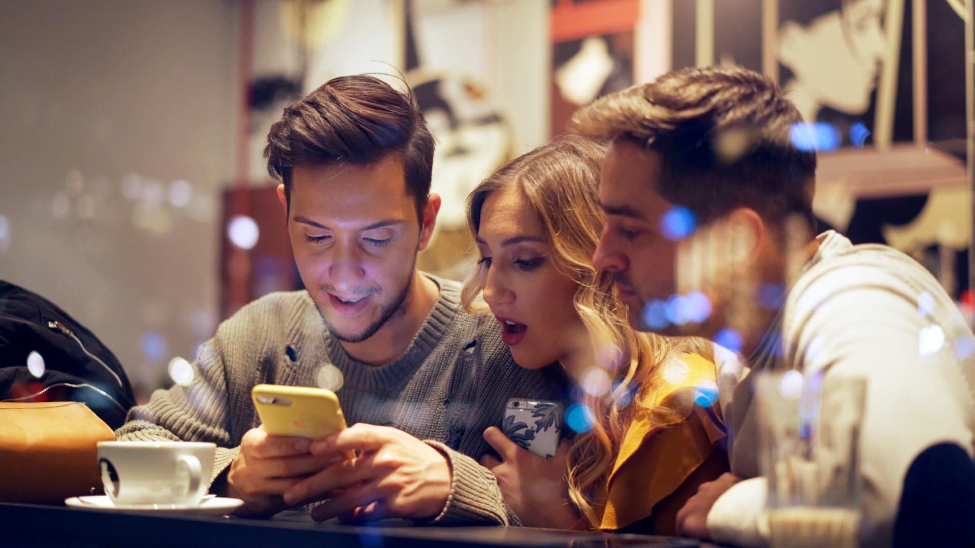 Amigos en una cafetería mirando el móvil sorprendidos